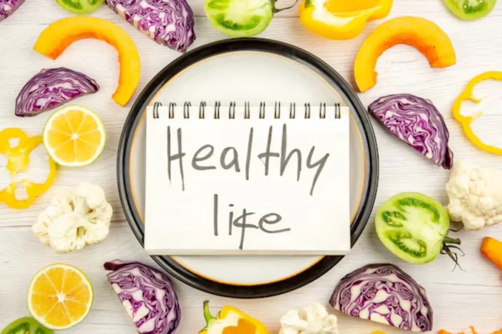 A notebook reading 'Healthy Life' surrounded by colorful vegetables like peppers, cabbage, and lemons