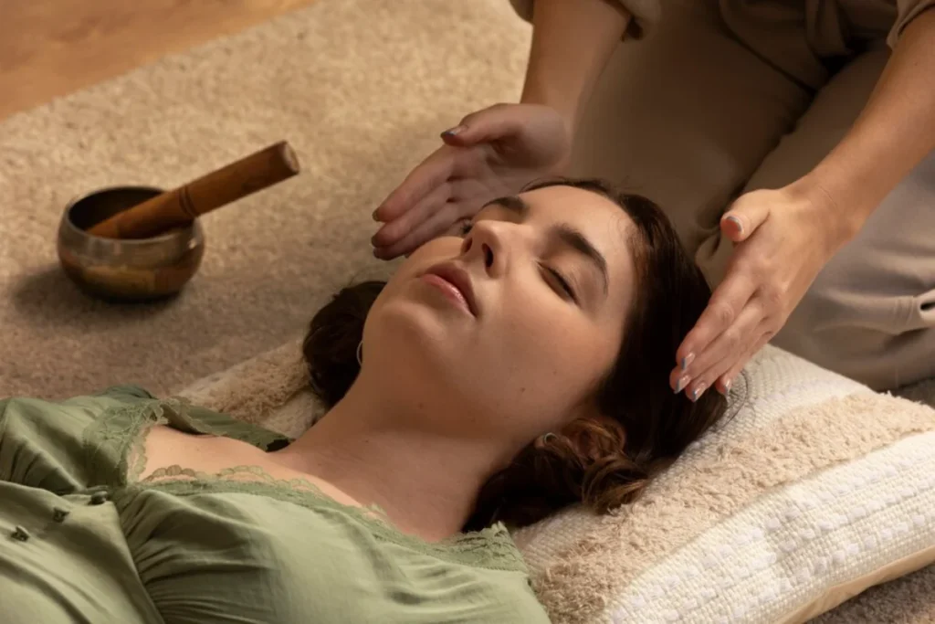 A woman receives a relaxing head massage in a serene setting with a singing bowl nearby.
