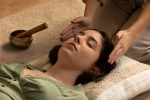 A woman receives a relaxing head massage in a serene setting with a singing bowl nearby.