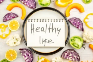 A notebook reading 'Healthy Life' surrounded by colorful vegetables like peppers, cabbage, and lemons