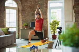 Man doing a yoga pose on a yellow mat in a stylish loft, filming himself with a camera.