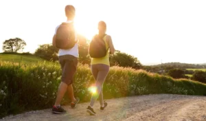 Two people hiking on a country path at sunset, surrounded by lush greenery.