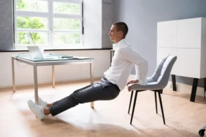 Man performing chair exercises in a modern office setting with a laptop on the desk.