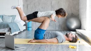 Father and son practicing yoga at home, with child balanced in the air on father's feet.