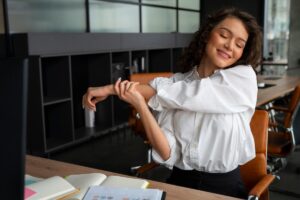 Woman stretching her arms with a satisfied expression at a modern office desk.
