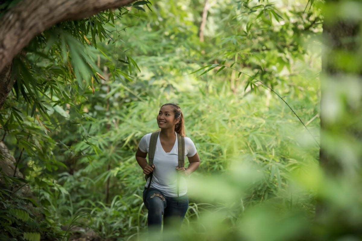  A young woman hiking through a lush forest, looking up and smiling.