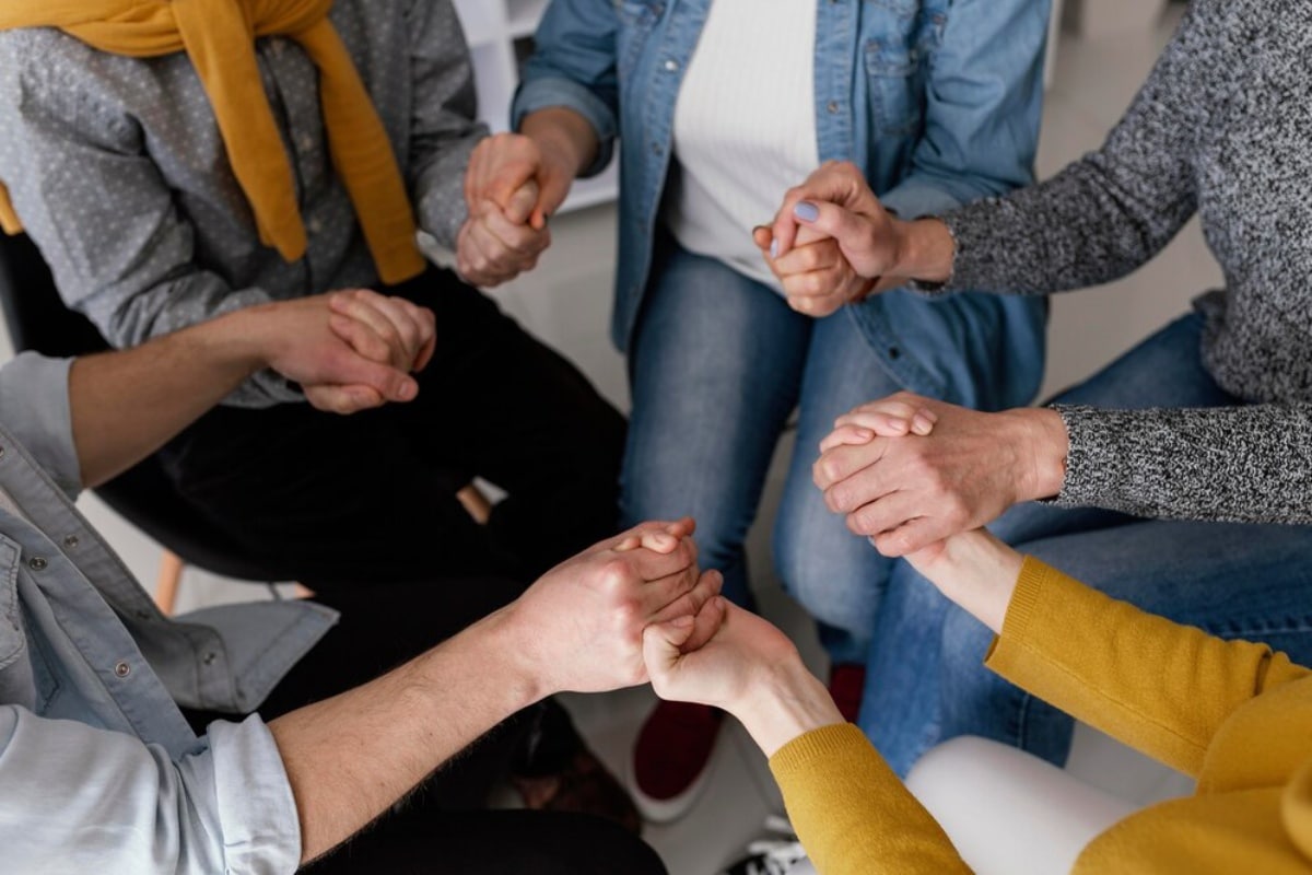 Group of people sitting closely, holding hands in a show of support and unity.
