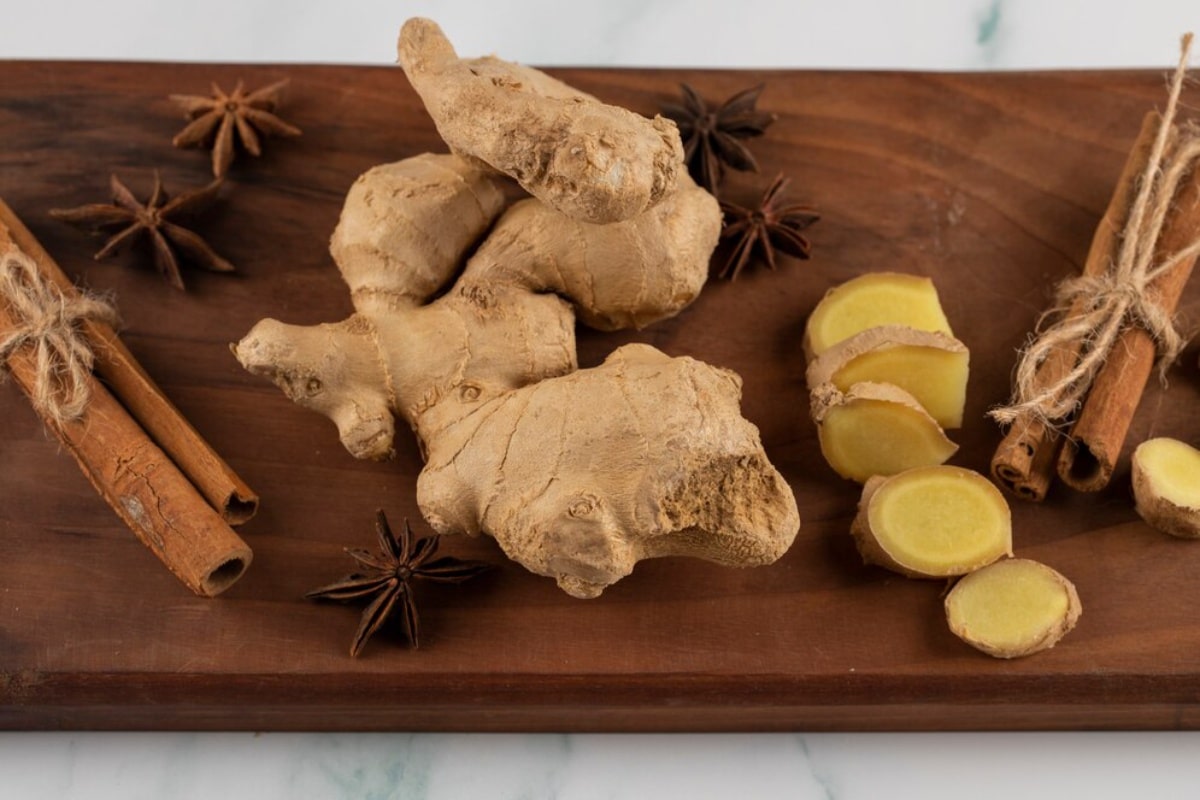 Whole and sliced ginger with cinnamon sticks and star anise on a wooden tray.