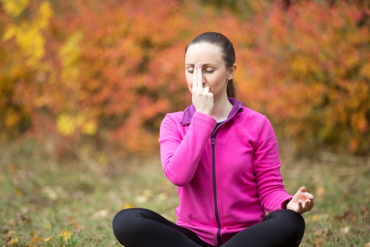 Woman in pink jacket meditating in autumn park, practising a breathing exercise.