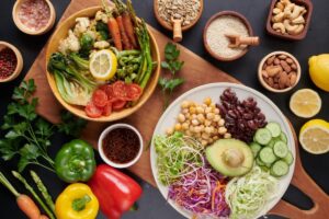 Assorted fresh vegetables, nuts, and grains neatly arranged on a dark background, highlighting a colourful and healthy meal setup.