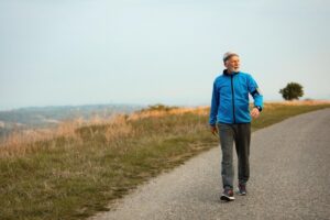 Elderly man in a blue jacket walking on a countryside path, enjoying a sunny day.